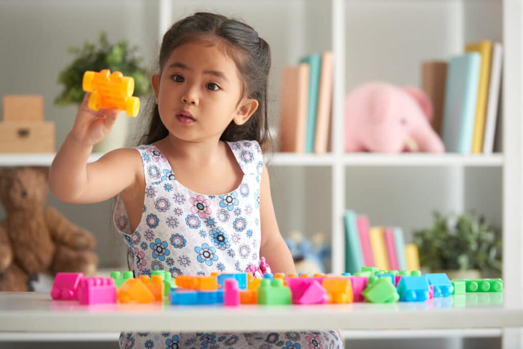 Young girl playing with colorful building blocks at home.