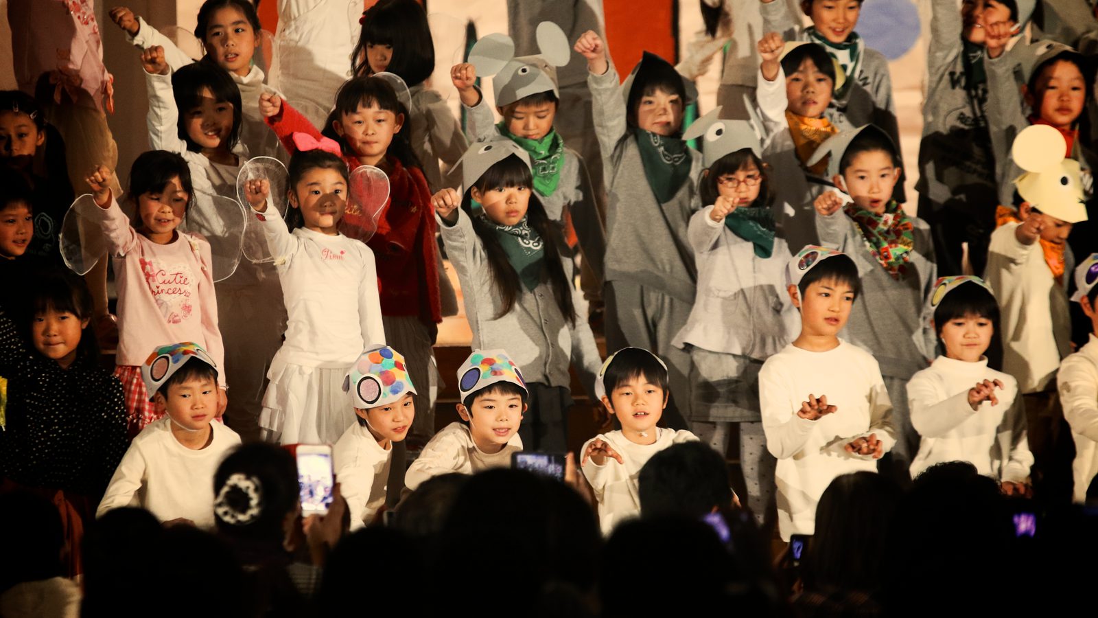 A hall full of children cheering in costume at a school play